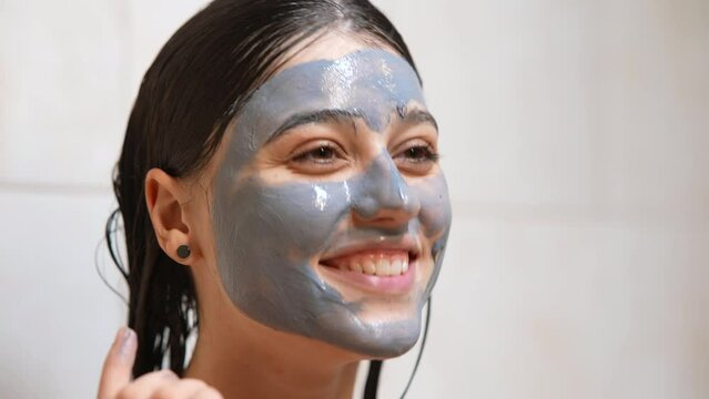 Skin care. Young woman applying clay green mask on her face.