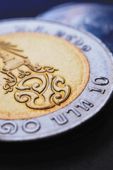 Translation: 10 baht Thailand. Thai coin of 10 baht lie on dark surface closeup. News about money....