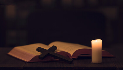 holy bible, lit candle and a cross on the table in the dark. 