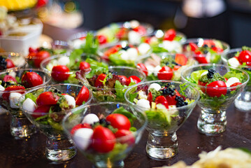 Small cocktail servings of cherry tomato salad, mozzarella balls, lettuce Lollo Rosso. Lots of portions in a glass serving. Catering Layout.