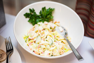 A plate of crab salad on the buffet table. Salad of fresh cucumbers, crab sticks, white beans, iceberg lettuce leaves, Lola rossa. Dressed with mayonnaise.