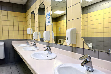 Public toilet minimalistic interior. A row of ceramic washbasins with a metal surface, a soap...