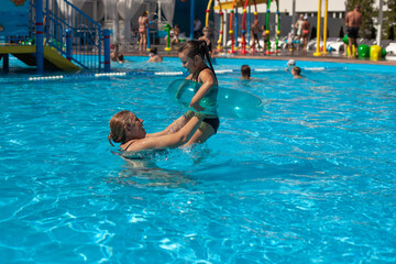 Naklejka premium Grandmother and granddaughter in the pool. A young grandmother throws a girl in an inflatable circle over the surface of the water in the hotel pool on a summer vacation. 