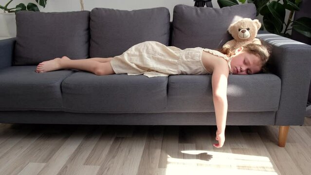 Cute little preteen girl sleep dream nap on cozy couch lying in comfortable pose with closed eyes. Tired tween child kid asleep on comfy sofa in silent light living room after active day. Sweet dreams