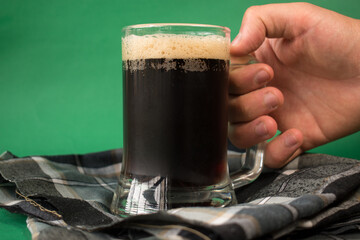 Hand taking a glass of black cold beer on green background