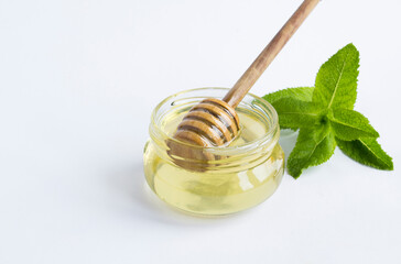 Closeup on honey on the glass jar and green mint on the white background. Copy space. © Liudmyla