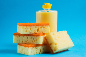 Dishwashing liquid in a transparent plastic bottle and porous yellow cleaning sponges on a blue background. The concept of ecological detergents