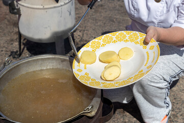 The cook drops potatoes from the plate into the cauldron in which fish soup is cooked