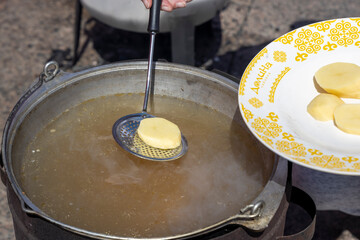 The cook drops potatoes from the plate into the cauldron in which fish soup is cooked