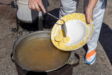 The cook drops potatoes from the plate into the cauldron in which fish soup is cooked