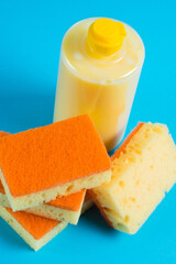 Dishwashing liquid in a transparent plastic bottle and porous yellow cleaning sponges on a blue background. The concept of ecological detergents
