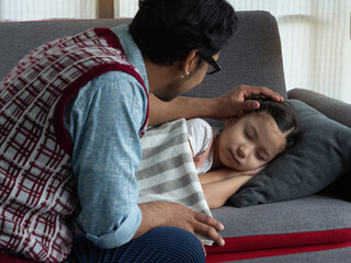 Father lovingly tuck cute little daughter to sleep on sofa in the living room at home. Daddy...