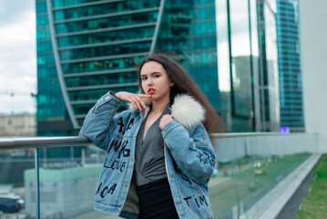 Fototapeta premium A fashionable girl with a wavy hairstyle and red lips poses on the street.