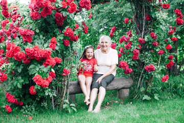 grandmother and granddaughter frolic and indulge in the garden on a bench under a rose.