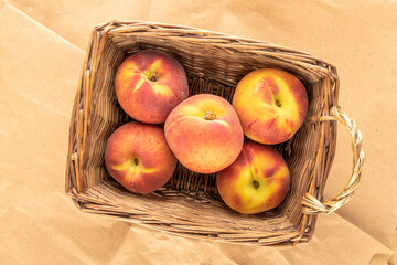 Several juicy ripe peaches in a basket on craft paper, close-up, top view.