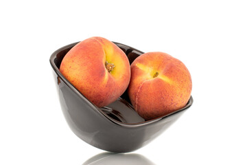 Two sweet organic peaches in a black ceramic dish, close-up, isolated on a white background.