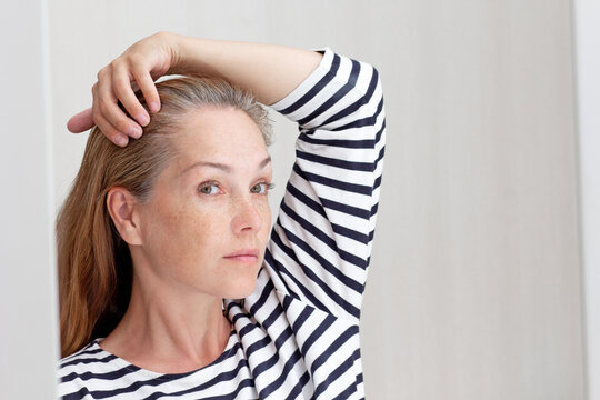 Beautiful 40s Woman Looking At Gray Hair In Mirror Reflection On Growing Out Root