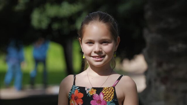 Cute little girl stands in the park and looks in the camera