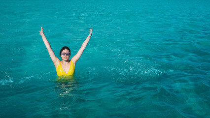A young woman in a yellow swimsuit is bathing in the azure sea, beautiful clear water. Vacation on a tropical island