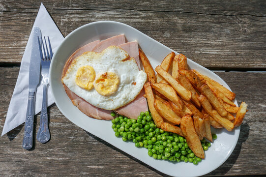 English pub grub. Food on plate on wooden table. Gammon ham, eggs and chips meal with peas. high calorie food 