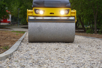 The road roller moves along the road under construction, leveling and compacting the gravel.