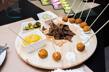 Plate with appetizers, catering service. Falafel balls on cream sauce. Sautéed spreads and rye breadcrumbs on a round wooden plate.