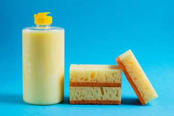 Dishwashing liquid in a transparent plastic bottle and porous yellow cleaning sponges on a blue background. The concept of ecological detergents