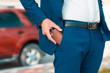 A businessman in a blue suit get a leather key bag from the pants. Defocused car on the background....