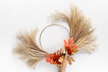 Dried floral wreath from dry pampas grass and Autumn leaves. Fall fecorations tied with cord to metal frame. Fig fruits on off white background. Natural sunlight.