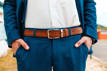 Man in an elegant suit with a leather belt on his trousers poses on the street. Close-up of the hands. The concept of style, business and luxury - obrazy, fototapety, plakaty
