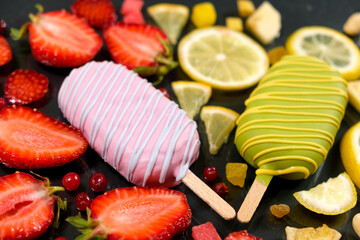 Two ice creams on a sticks - strawberry and lemon on a black background. Summer fruit desserts.