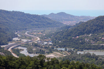 Obraz premium A highway in a picturesque mountainous area along a clear blue river. Sochi, Krasnaya Polyana, Russia.