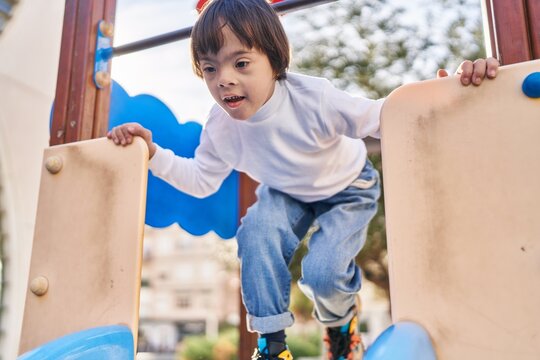 Down syndrome kid smiling confident playing on slide at park