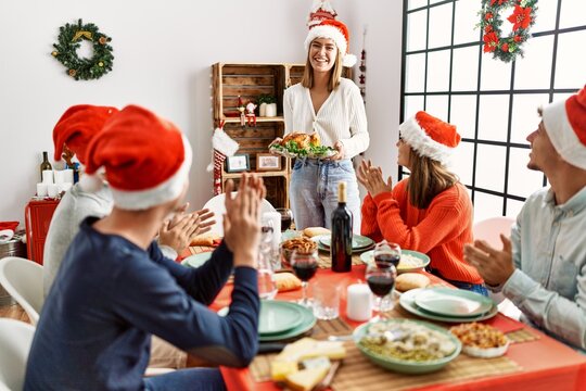 Group of people meeting clapping and sitting on the table. Woman standing and holding roasted turkey celebrating Christmas at home