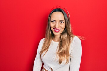 Beautiful hispanic woman wearing red diadem looking away to side with smile on face, natural expression. laughing confident.