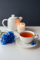 Obraz na płótnie Canvas Tea, teapot, candle and a bouquet of cornflowers on the table