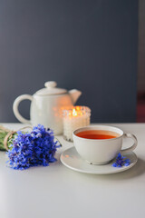 Tea, teapot, candle and a bouquet of cornflowers on the table