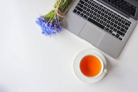 Office desk table with laptop computer with black screen, tea, flowers on white background top view