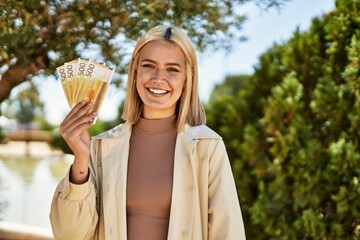 Young blonde girl smiling happy holding norway krone banknotes at the city.