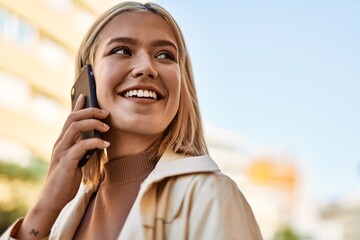 Young blonde girl smiling happy talking on the smartphone at the city.