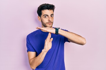 Young hispanic man wearing casual t shirt doing time out gesture with hands, frustrated and serious...