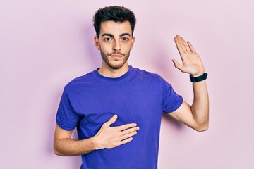 Young hispanic man wearing casual t shirt swearing with hand on chest and open palm, making a...