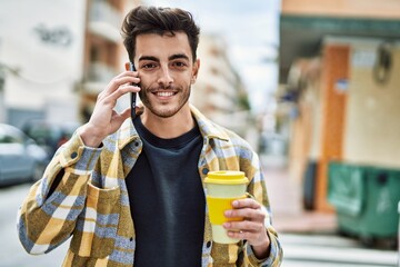 Handsome hispanic man smiling happy and confident at the city speaking on the phone and drinking a...