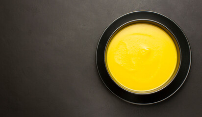 Top view of pumpkin soup in the black bowl on the dark surface with copyspace
