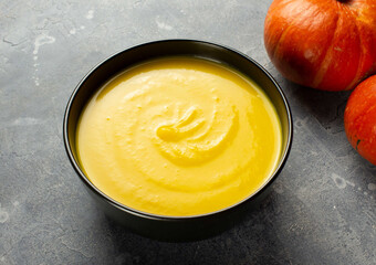 Pumpkin cream soup in the black bowl on the grey surface with pumpkins
