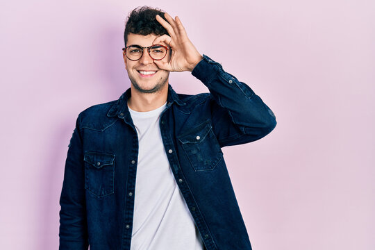 Young hispanic man wearing casual clothes and glasses doing ok gesture with hand smiling, eye looking through fingers with happy face.