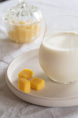 A glass of milk on a table with a white tablecloth. Glass jar with honey and yellow candies.