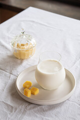 A glass of milk on a table with a white tablecloth. Glass jar with honey and yellow candies.