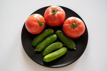 fresh tomatoes and cucumbers on a black plate on the white kitchen table 