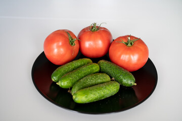 fresh tomatoes and cucumbers on a black plate on the white kitchen table 